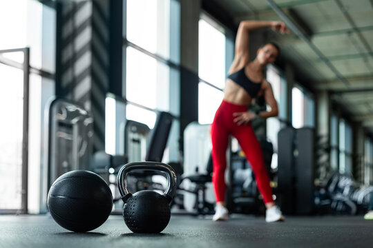 Fit woman in red leggings warming up before gym workout near kettlebell and medicine ball