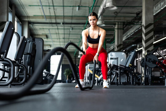 Athletic woman in red leggings doing intense battle ropes workout in gym