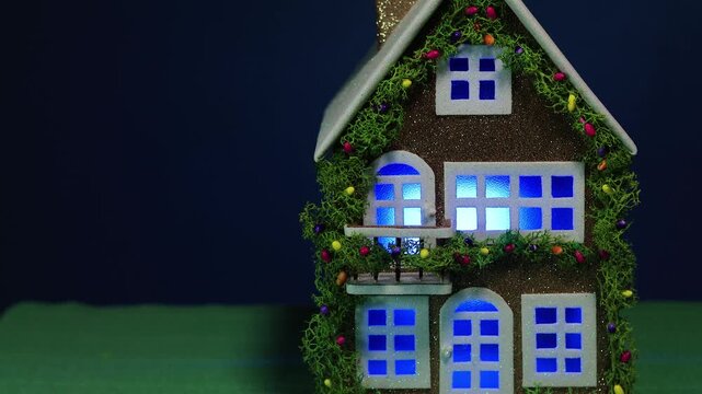 On a dark blue background and green covering, a fairytale decorated house with color-changing light in the windows