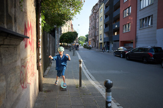 Young boy in helmet rides skateboard on sidewalk in European city street