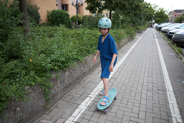Young boy in blue outfit and helmet rides a skateboard on a paved path © 4Max