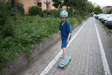 Young boy in blue outfit and helmet rides a skateboard on a paved path © 4Max