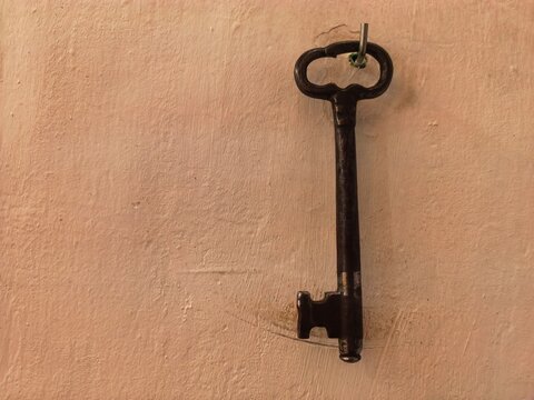 Old-fashioned door key hanging on a hook against an aged brown wall, rustic vintage interior detail.