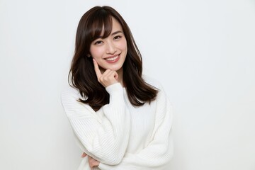 Fototapeta premium 白いセーターを着た笑顔の若い日本人女性が頬に指を当てる