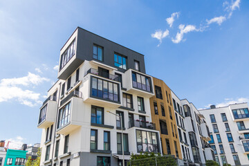 Fototapeta premium Modern apartment building facade with white and dark grey panels under blue sky. Urban