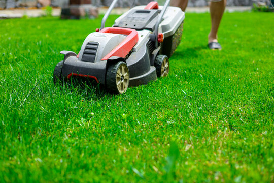Mow lawn concept. Low angle of a man pruning horticulture or hedge lawnmower machine cutting or trimming grass outdoors in his backyard on a sunny summer day. House maintenance work, leisure activity