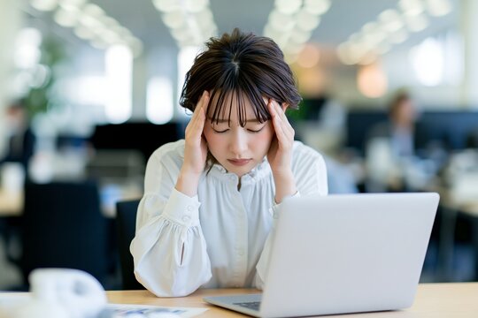 疲労困憊で頭痛に悩むオフィスワーク中の日本人女性