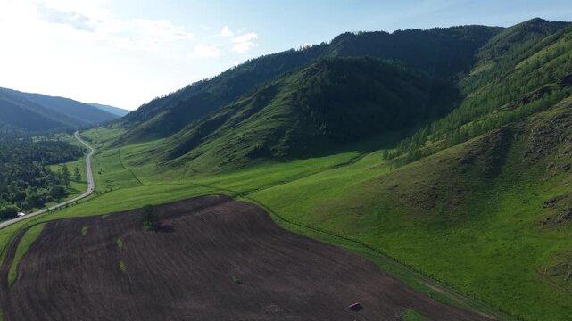 A cinematic drone aerial video flying forward and smoothly rising over a cultivated valley field to refocus on a steep green mountain ridge near Seminsky Pass.