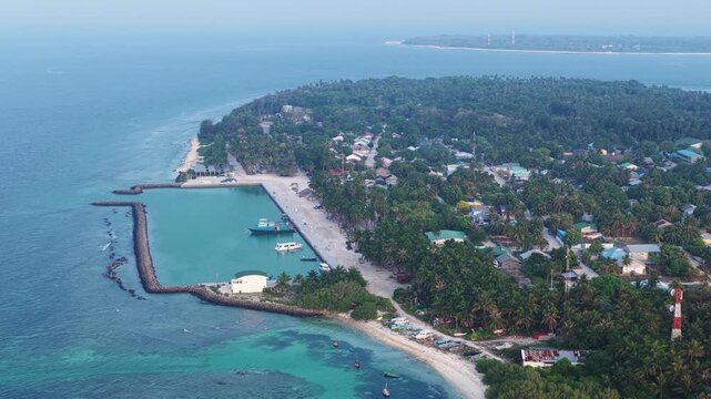 Aerial view of the tropical island of Vaikaradhoo featuring a protected harbor with boats, lush palm trees, and turquoise waters in Vaikaradhoo, Haa Dhaalu Atoll, Maldives.