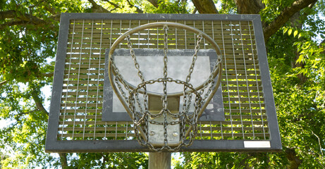 Street basketball hoop with chain net against green trees background © Olena