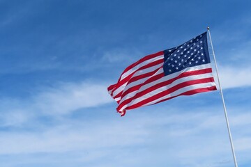 Obraz premium Fluttering American flag against blue sky and clouds