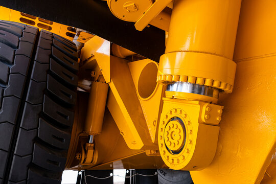 Tight close-up showing the yellow painted suspension components and large tire of heavy construction machinery. Visible elements include a hydraulic hinge