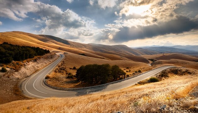 winding road curving through a scenic mountain range landscape showcasing a journey through diverse natural terrain with dry grass hills and scattered trees under a cloudy sky