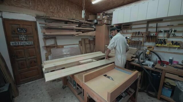 Authentic cabinetmaker sorting long pine timber boards on a wooden workbench inside a cluttered domestic garage workshop wide establishing shot of a real home improvement diy woodworking project