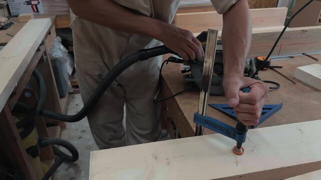 Skilled handyman securing timber board with clamp and positioning handheld circular saw using try square guide in bright rustic workshop authentic documentary b-roll