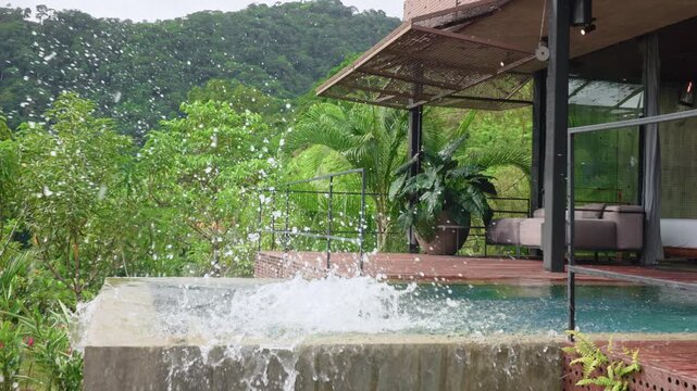 Slow motion footage of young boy jumping into infinity pool at luxury tropical resort. Water splashes dramatically as child lands in turquoise water with lush green rainforest mountains in background.