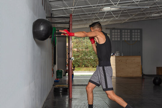 Young Hispanic boxer performing medicine ball wall throw in gym
