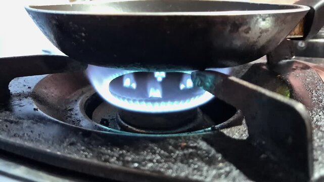 Horizontal low angle close up shot of igniting a kitchen gas stove burner with a steady bright blue flame heating a frying pan.