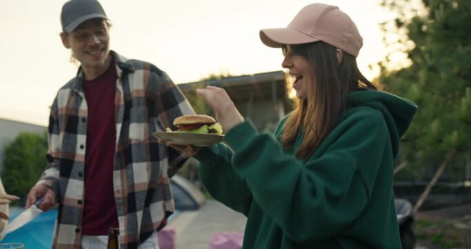 Smiling young woman gesturing beside man with plate outdoors