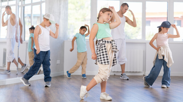 Expressive preteen girl honing hip hop dance moves in sunlit choreographic studio setting during training with group of children and teacher