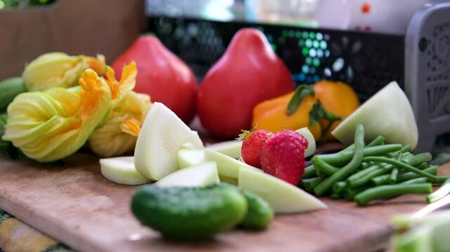 Freshly washed vegetables are prepared on a wooden board before cooking. Clean pattypan squash, cucumbers, green beans, tomatoes, and young zucchini are sliced in warm sunlight.