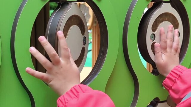 Child's hands playing tic-tac-toe on an interactive playground panel, rotating round discs. Concept of developing fine motor skills, logical thinking, and outdoor 