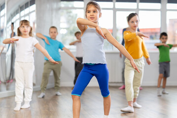 Fototapeta premium Girls with boys repeat teaches sequences of movements during training, train to perform electro dance, enjoys active hobby to favorite music. Unrecognizable female teacher administer conduct class