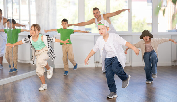 Expressive preteen boy honing hip hop dance moves in sunlit choreographic studio setting during training with group of children and teacher..