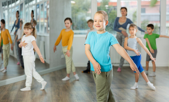 Boy learns to dance during childrens master class in studio. Teacher watches students, participates in training