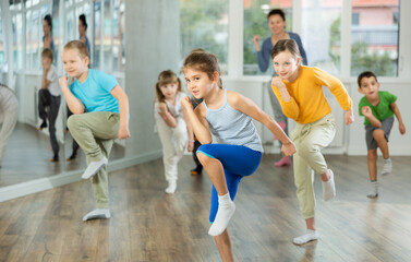Fototapeta premium Girls with boys repeat teaches sequences of movements during training, train to perform hip hop, enjoys active hobby to her favorite music. Unrecognizable female teacher administer conduct class