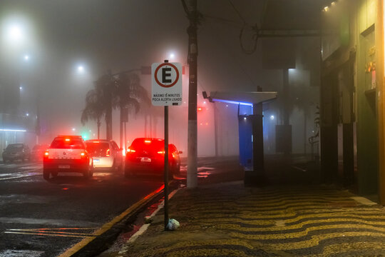 A car drives through thick fog on an urban street under traffic lights at night in downtown Marilia, Sao Paulo state, 