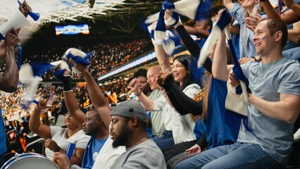 Diverse blue football supporters raising arms and chanting together, in stadium stands during live soccer match with powerful crowd energy. © DC Studio