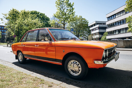 Hanover, Germany - April 22, 2026: Orange vintage Volkswagen sedan parked on a tree-lined street in Hanover under clear blue sky