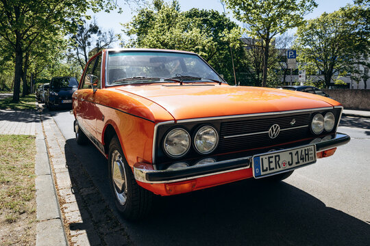 Hanover, Germany - April 22, 2026: Orange vintage Volkswagen sedan parked on a tree-lined street in Hanover under clear blue sky