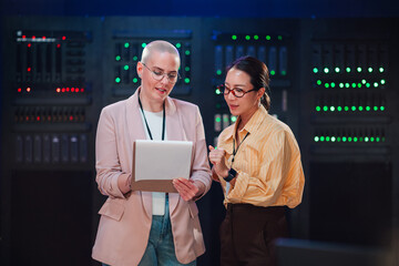 Fototapeta na wymiar Two women engineers standing in a server room, discussing data operations and advanced technology for it management