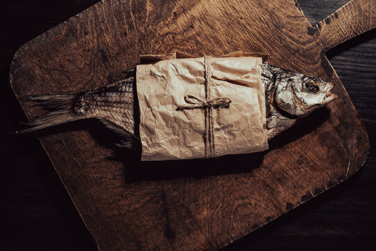 Whole dry salted bream wrapped in eco friendly brown paper on rustic cutting board. Traditional beer snack flat lay for pub menus, local seafood markets or authentic food packaging mockups