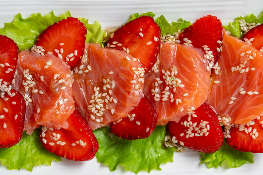 Gourmet salmon tataki salad with strawberry slices and sesame seeds on lettuce. Beautiful texture backdrop for restaurant menu catering promotion or exotic recipe blog