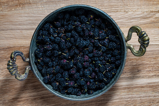 Fresh organic black mulberries in a rustic vintage bowl. Ripe sweet mulberries inside an antique metal pot on a wooden table, closeup