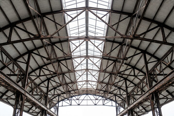 Fototapeta premium Low angle view looking up at the complex metal trusses and skylights of a vast industrial roof