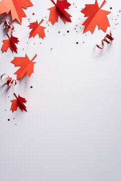 Red paper maple leaves and curled ribbon for Canada Independence Day celebration on white vertical background