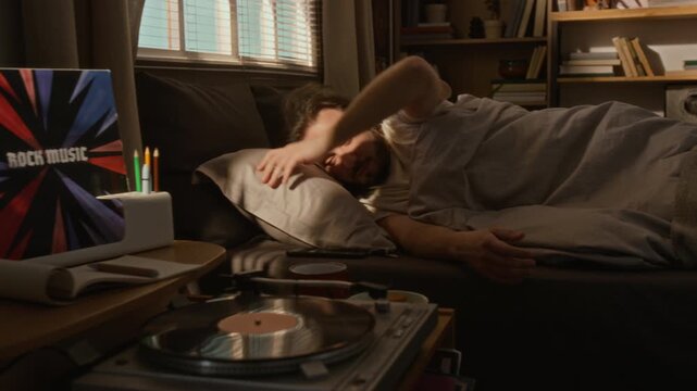 Young adult Caucasian man waking up in bed, shielding eyes from sunlight, and checking smartphone to turn off alarm. Perfect for morning routine, digital wellness, or mobile app marketing campaigns