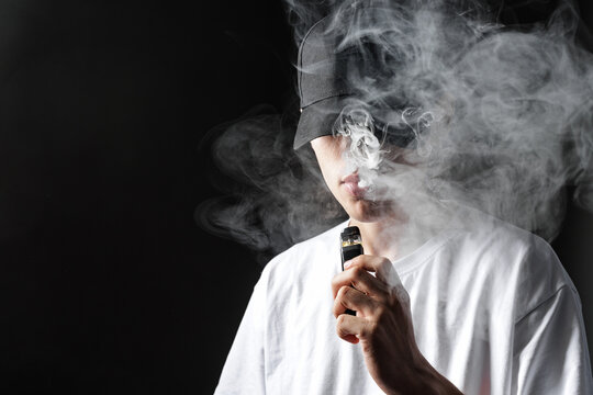 Vaper Exhaling Smoke with a Vape Device in a Dark Setting