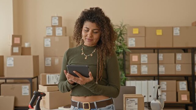 Woman holding tablet and tapping screen, midriff visible, surrounded by parcels in a building; focused entrepreneurship.