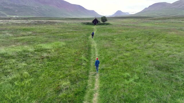 Aerial view of two people walking along a path towards the historic turf-roofed Grafarkirkja church surrounded by green fields in Hofsos, Skagafjordur, Iceland.