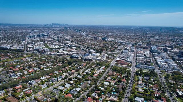 Wide aerial view of a vast metropolitan city with dense residential neighborhoods and commercial districts stretching towards the horizon under a clear blue sky on a bright day