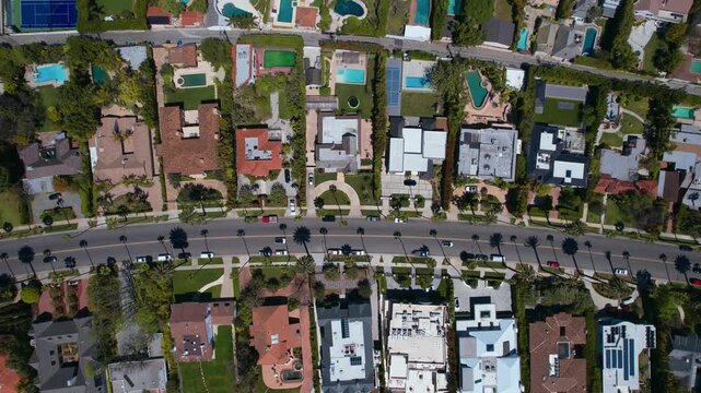 Aerial top-down view of a luxury suburban residential neighborhood with swimming pools, lush green lawns, and modern houses along a curved street under bright sunny daylight in a coastal city
