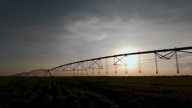 Silhouette of a large center pivot irrigation system spanning across a vast agricultural field at sunset, highlighting modern farming technology and water management in a rural landscape