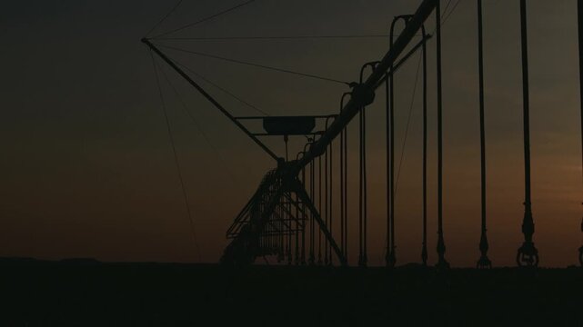 Silhouette of a large center pivot irrigation system in a vast farm field during a dramatic sunset, highlighting modern agricultural technology and water management in rural landscapes