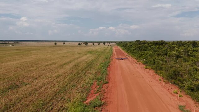 Wide aerial view of a long red dirt road stretching through vast agricultural fields and green vegetation under a cloudy sky in a rural countryside landscape during daytime