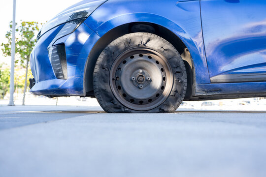Flat Tire on Blue Car Parked on Street. A close up view of a deflated vehicle tire on a sunny day depicting an automotive emergency or a mechanical failure requiring repair and roadside assistance